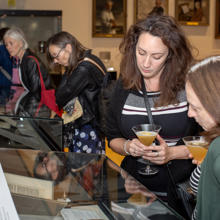 Two Visitors With Drinks Looking At The Healing Words Exhibition