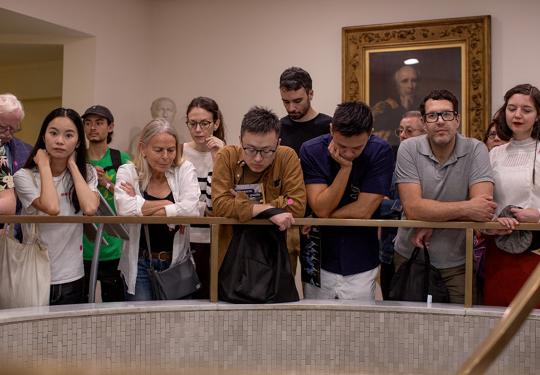 A tour group leans over a brass banister in the RCP
